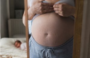 Madre observando su barriga después del parto frente al espejo
